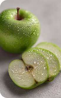 Green apple with water droplets and a sliced green apple on a gray surface