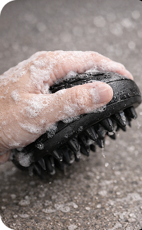 Hand holding a black massage brush with foam on a textured surface