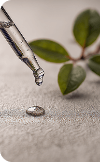 Dropper with a drop of liquid on a textured surface with green leaves in the background