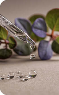 Close-up of a dropper with clear liquid on a surface with green leaves in the background