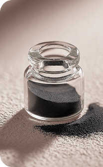 Small glass jar filled with black sand on a textured surface