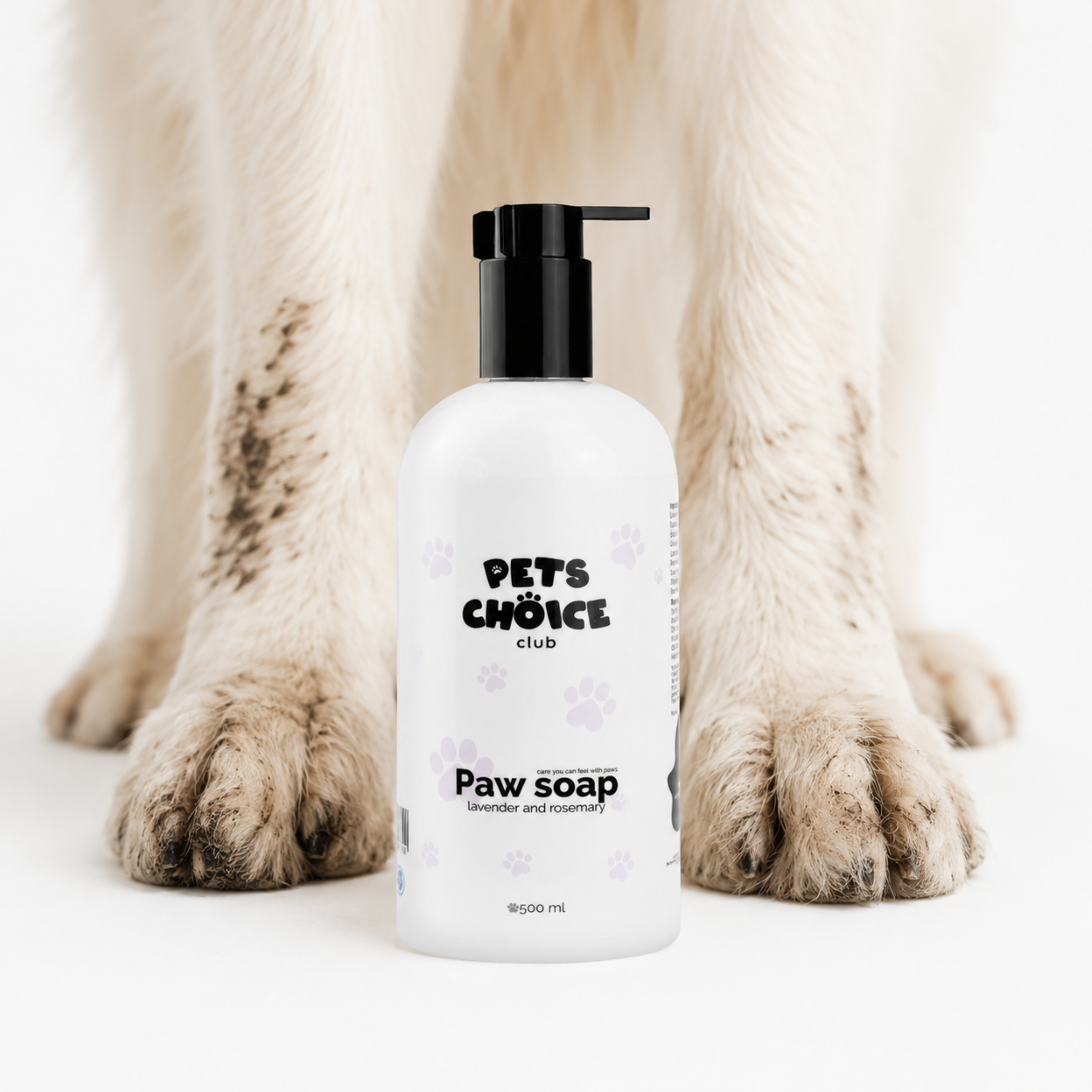 A white bottle of 'Paw soap' by 'Pets Choice Club' with a black pump dispenser, positioned in front of a dog's legs and paws on a clean white background.