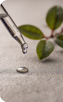 Dropper with a drop of liquid on a textured surface with green leaves in the background