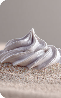 Close-up of a swirl of white frosting on a textured surface with a gray background