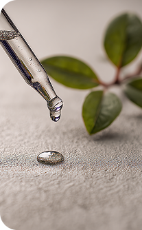 Dropper with a drop of liquid on a textured surface with green leaves in the background